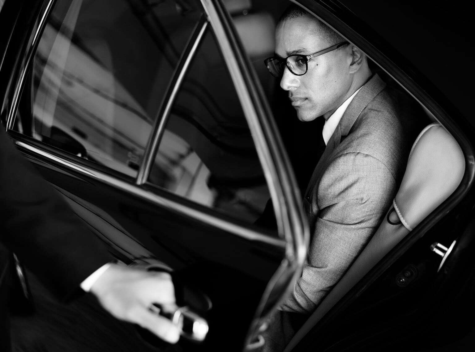 Photo of a man seated in the rear seat of a car while the driver closes the door