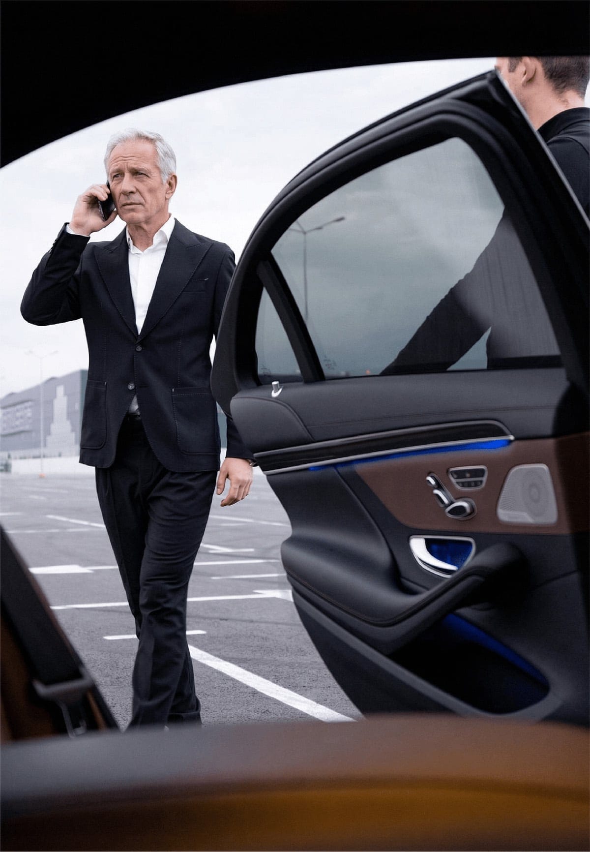 Photo of a man on the phone getting into an official car while the driver holds the door open